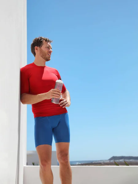 Atleta hombre corredor beber deportes agua botella entrenamiento en casa balcón o gimnasio al aire libre agotado tener golpe de calor. Cultivo vertical de cuerpo muscular de personas activas estilo de vida —  Fotos de Stock