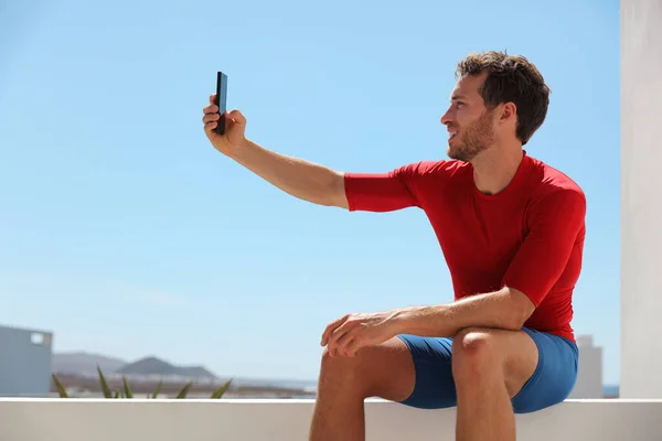Atleta de fitness hombre selfie tomando una foto con teléfono móvil fuera en el balcón de casa o gimnasio para las redes sociales. Estilo de vida joven activo —  Fotos de Stock