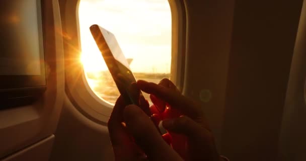 Téléphone gros plan des mains de la femme en utilisant un téléphone portable assis dans l'avion. Coucher de soleil et fusée éclairante dans le siège de fenêtre. Concept de téléphone portable dans l'avion — Video