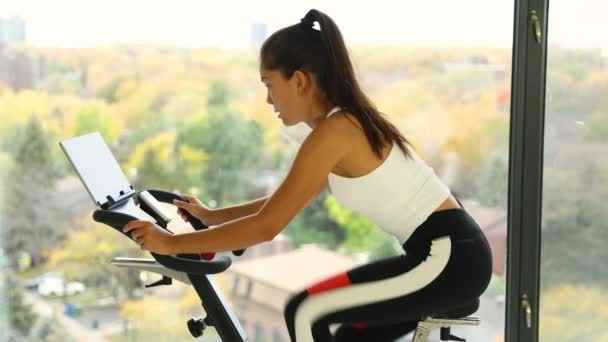 Ekranla bisiklet sporu yapmak için evde egzersiz yap. Sabit bisiklet eğitimi alan kadın, kardiyo çalışması için online video dersi izliyor. — Stok video