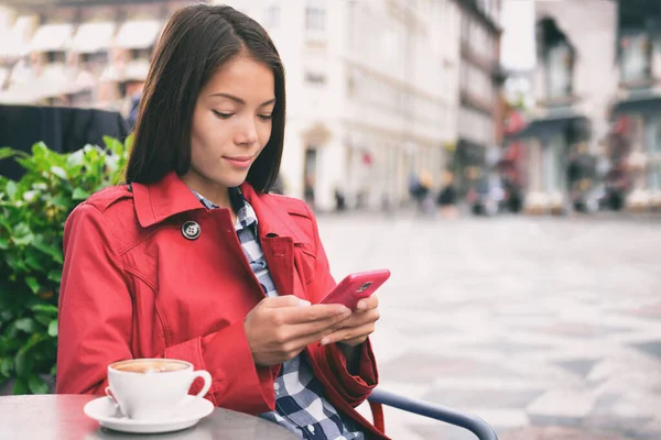 Cafe woman using mobile phone drinking cappuccino coffee at outdoor street european city. Europe travel lifestyle. Asian businesswoman in fashion red trench coat — Stock Photo, Image