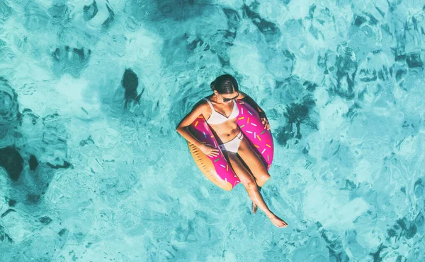 Praia férias verão diversão menina relaxante na piscina flutuante anel de donut colchão de ar flutuando no fundo azul do oceano, vista superior da antena — Fotografia de Stock