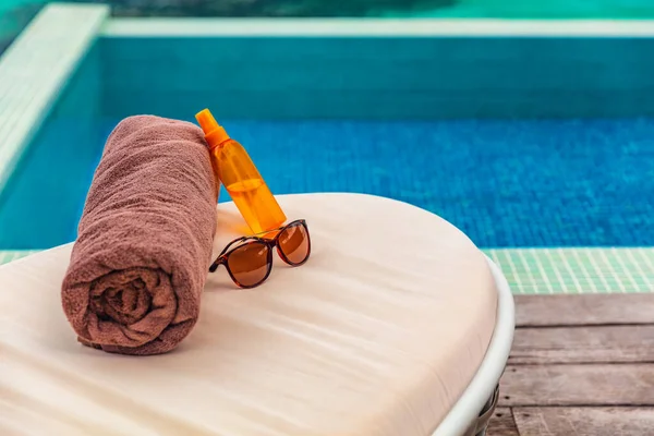 Fondo de la piscina del hotel de vacaciones de bronceado con accesorios de viaje para broncearse en las tumbonas vacaciones en destino caribeño. Aceite de bronceado, toalla y gafas de sol mujeres objetos —  Fotos de Stock