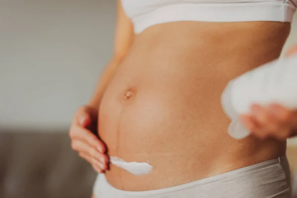 Pregnant woman putting cream on first trimester belly for stretch marks skin care prevention. Moisturizing dry skin during winter — Stock Photo, Image