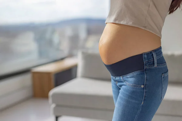 Vêtements de maternité femme enceinte portant des jeans extensibles full panel stretch pendant la grossesse à la maison. Gros plan sur la bosse et les vêtements — Photo
