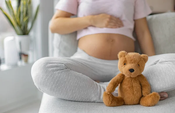 Graviditet. Gravid kvinna bär moderskap kläder avkopplande på soffan med nalle baby leksak i fokus för baby shower gåva koncept eller väntar ett barn — Stockfoto