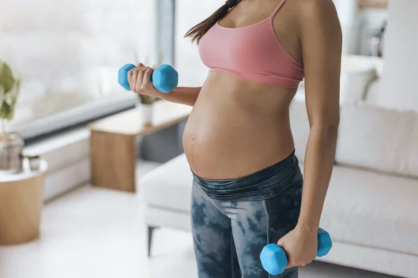 Hamile kadın evde egzersiz yapıyor. Kol ağırlıklarıyla beden eğitimi eğitimi egzersizi. Vücut çalışması kol kıvrımları karın ve kollara yakın. — Stok fotoğraf