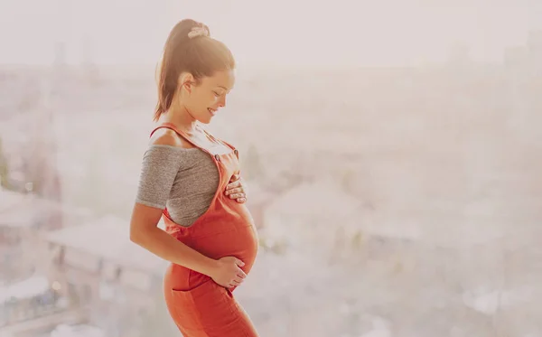Mujer embarazada asiática feliz tocando su bulto del embarazo para la sesión de fotos prenatal con ropa de maternidad overoles. Hermosa joven modelo multirracial chica — Foto de Stock