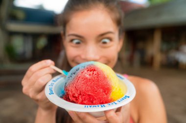 Hawaiian shave ice happy woman tourist making funny face hungry eating sweet frozen snow cone local dessert food of Hawaii clipart