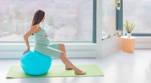 Zwangere vrouw stabiliteit bal prenatale zwangerschap thuis training stretching spieren voor de geboorte met behulp van geboortebal voor de bevalling positie en weeën verlichting — Stockfoto