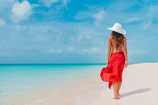 Lüks plaj tatili zarif turist kadın kırmızı plaj elbisesi ve güneş şapkasıyla beyaz kumlu Karayip plajında yürüyor. Tatil köyündeki bayan turist. — Stok fotoğraf