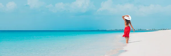 Mujer de vacaciones en la playa caminando en vacaciones de verano Vacaciones en el Caribe con sombrero blanco y falda sarong. Fondo de la bandera panorámica del océano. Elegante turista dama — Foto de Stock