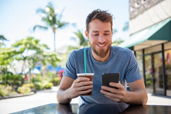 휴대 전화 전자 기기를 사용하는 젊은이는 카페 문자 메시지와 함께 휴대폰을 들고 여름에 커피를 마시는 앱을 사용 한다. 건방진 젊은 남자가 스마트폰으로 행복하게 웃고 있습니다. 도시의 수컷 — 스톡 사진