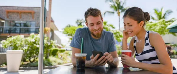 Amigos o pareja interracial citas hablando en la cita de café sentado en la mesa del café con fotos de aplicaciones de teléfono móvil beber café en verano. Hombre joven usando teléfono inteligente sonriendo feliz a la mujer asiática —  Fotos de Stock