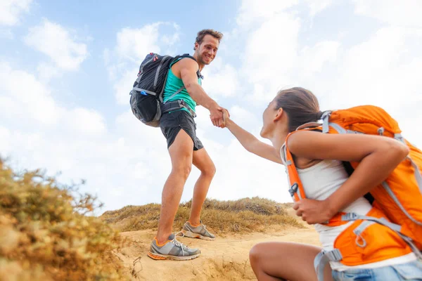 女性が山のハイキングで丘を登るのを助ける人々はハイキングをする。手のチームは、女の子のための成功のトレッキングをサポートする友人をサポート — ストック写真