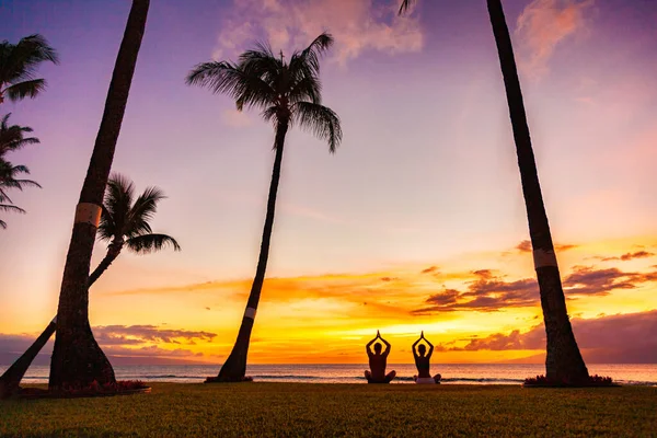Yoga retreat στις τροπικές καλοκαιρινές διακοπές διαλογισμό άνθρωποι ζευγάρι διαλογισμό σε lotus ποζάρουν με τα χέρια προσευχή στο ηλιοβασίλεμα λάμψη σιλουέτες στην παραλία — Φωτογραφία Αρχείου