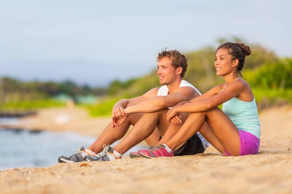 Spor yaptıktan sonra plajda günbatımının tadını çıkaran zinde insanlar. Spor salonundaki aktif çift kadın ve erkek tatilde. Seyahat plaj tatili — Stok fotoğraf