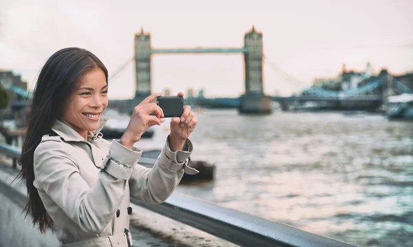 A londoni turista nő a Tower Bridge-et fotózza. A londoni nő mobiltelefonos kamerával fényképez. Lány élvezi a kilátást a Temze folyóra, London, Anglia, Nagy-Britannia. Egyesült Királyság turizmus. — Stock Fotó