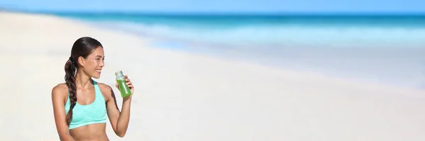 Fitness running woman drinking green smoothie juice bottle on beach landscape banner background. Atleta saudável vida ativa em dieta de desintoxicação agitação probiótica panorâmica — Fotografia de Stock