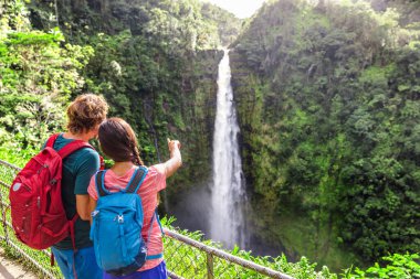 Couple tourists on Hawaii by waterfall. Tourist girl pointing at Akaka Falls waterfall on Hawaii, Big Island, USA. Travel tourism young people concept clipart