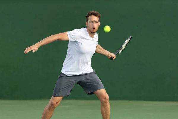 Tennis player man hitting ball with racket on green background. Sports athlete training forehand grip technique on outdoor court — ストック写真
