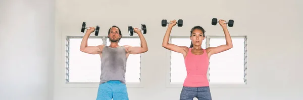 Fitness gym couple training arms with dumbbells in indoor class working out overhead shoulder press with weights or standing dumbbell press exercise. Banner panorama fit people lifestyle — ストック写真