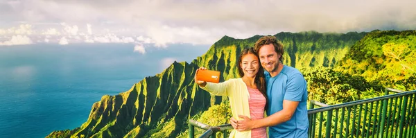 Reizen selfie paar bij Napali Kauai Hawaii banner. Jonge toeristen bij Na Pali Coast kijken uit naar mobiele telefoon selfie smartphone foto. Reizigers op Hawaïaans landschap, panorama gewas — Stockfoto