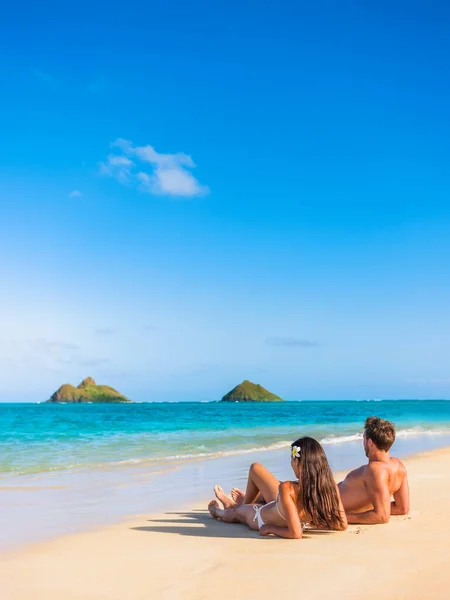 Beach vacation couple relaxing sunbathing on hawaiian tropical beach in Lanikai, Oahu, Hawaii, USA. American people on summer holidays sun tanning lying down on sand — стоковое фото