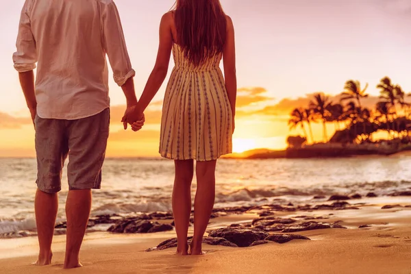 Strand koppel kijken naar zonsondergang hand in hand. Mensen van achteren ontspannen genieten van zomervakantie op tropische bestemming — Stockfoto