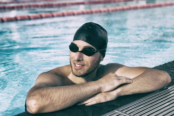 Homem atleta de natação usando óculos esportivos e boné na piscina interior — Fotografia de Stock