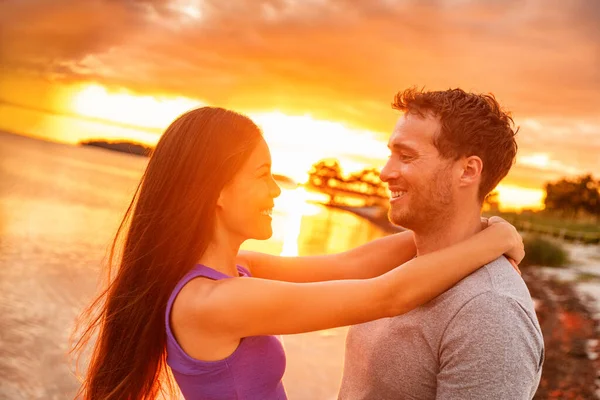 Par i kärlek skrattar vid solnedgången glöd på sommaren strand tropisk karibisk semester. Glad asiatisk kvinna ler mot en vit man — Stockfoto