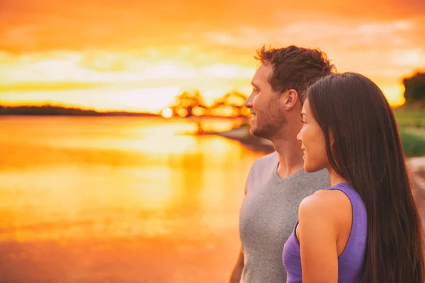 Casal relaxante na praia assistindo pôr do sol brilhar sobre o oceano em fundo caribenho. Asiático menina, caucasiano homem interracial relacionamento — Fotografia de Stock