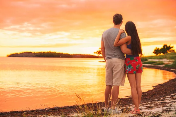 Paar ontspannen op zomervakantie reizen staan op het strand kijken zonsondergang in tropische bestemming. Silhouet bij schemering van achteren — Stockfoto