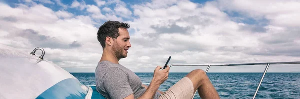 Yacht estilo de vida de luxo jovem usando banner panorama celular. Pessoa relaxante no convés mensagem SMS SMS no telefone móvel sob o sol férias de verão Fotografia De Stock