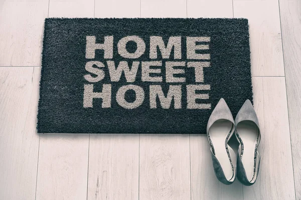 New condo front door mat top view. Modern living business woman high heel shoes on Home Sweet Home entrance doormat. Homeowner moving in concept. background concept. Fashion grey suede high heels. — ストック写真