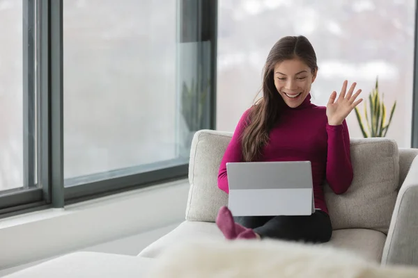 Working from home Asian woman on remote work online video meeting waving hello to her colleagues on webinar live videocall videoconference. Счастливая девушка сидит на диване в гостиной. — стоковое фото