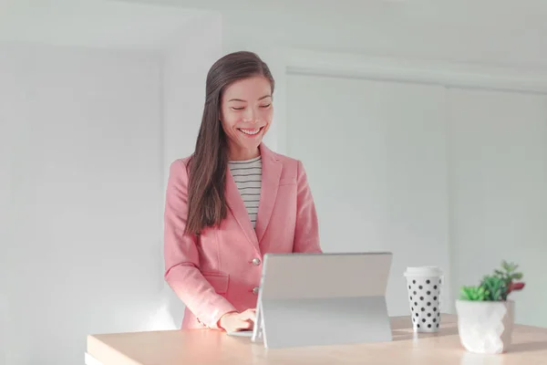 Fernarbeit Asiatin, die von zu Hause aus am Büro-Laptop am Stehtisch arbeitet. Glückliche Geschäftsfrau nutzt Computer für Online-Banking. Stockbild