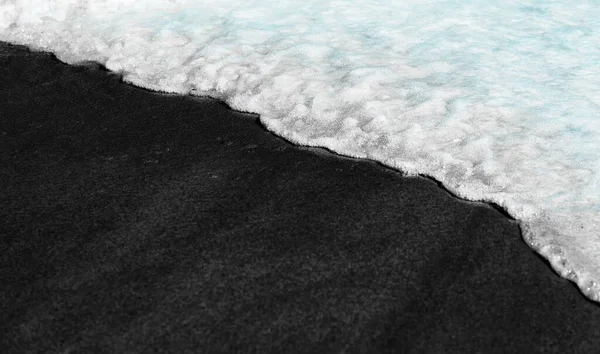 Black beach background waves black and white on volcanic sand texture washed over by water ocean wave tide. Serene idyllic ocean travel vacation concept banner — Foto de Stock