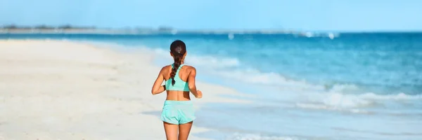 Running fitness on beach athlete runner running away doing high intensity interval training on summer workout. View from the back of woman panoramic — стоковое фото