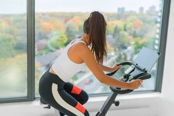 Trainieren Sie zu Hause Indoor Cycling mit Online-Unterricht auf dem Bildschirm. Frau trainiert Cardio-Radfahren auf Workout-Spin-Bike aktiven Fitness-Lebensstil — Stockfoto
