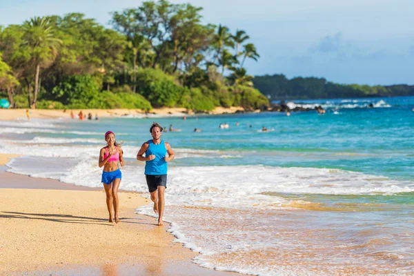 Bieganie sportowej pary sportowców ćwiczących na hawajskiej plaży robi ćwiczenia cardio hiit workout. mężczyzna i kobieta biegacze trening razem boso na piasku w falach — Zdjęcie stockowe