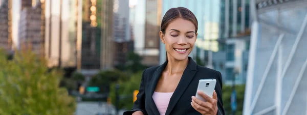 Woman sms texting using app on smart phone in city business district. Young business woman using smartphone smiling happy wearing suit jacket outdoors. Female professional in her 20s Panoramic banner. — Foto de Stock