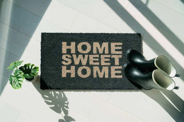 Rain boots on home sweet Home door mat during fall rainy season. Entrance doormat of house homeowner. Top view of rug for floor protection of rain water during autumn Stockbild