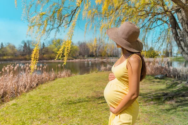 Pregnant woman walking in park wearing sun hat for skin solar protection against melasma skincare during summer. Pregnancy care — Stok fotoğraf
