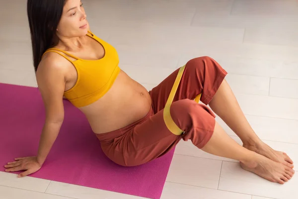 Zwangere vrouw training benen doen prenatale zwangerschap clamshell zittende heup oefening met weerstand banden voor te bereiden op de geboorte. Aziatisch meisje doen workout zittende pilates fitness oefeningen Rechtenvrije Stockafbeeldingen