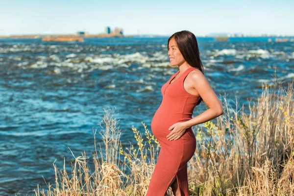 Retrato de maternidad de la mujer asiática durante el embarazo que sostiene el vientre embarazada contra el fondo natural del río. Paseo al aire libre en entorno natural — Foto de Stock