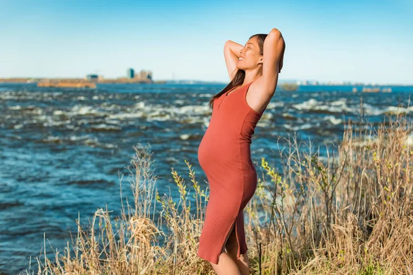 Pihentető terhes nő boldog a természetben. Terhesség életmód Ázsiai lány séta River Park élvezi a tiszta víz, levegő nyáron tavasszal. Emelje fel a kezét! — Stock Fotó