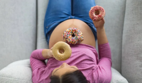 妊娠中の女性は腹に甘いドーナツを食べる 妊娠中のデザートや不健康な食べ物の渇望 妊娠糖尿病のための赤ちゃんのバンプ上のケーキの面白いトップビュー — ストック写真