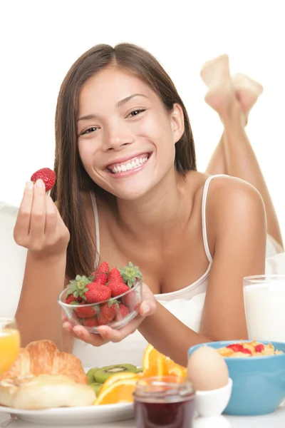 Νεαρή γυναίκα τρώει φρούτα με το πρωινό στο κρεβάτι — Φωτογραφία Αρχείου