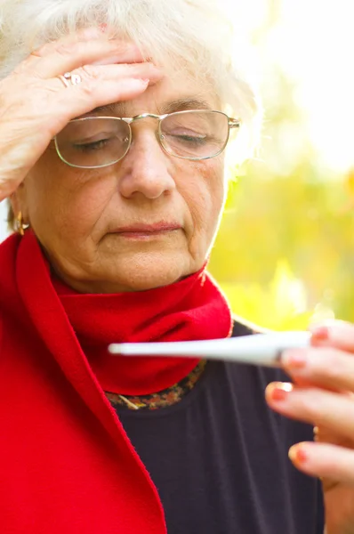 Old woman taking her temperature — Stock Photo, Image
